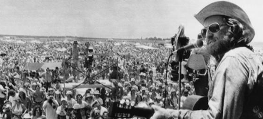 Willie Nelson playing in front of a large audience. Black and white image from the 70s.