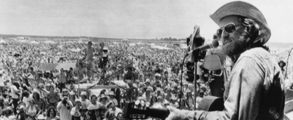 Willie Nelson playing in front of a large audience. Black and white image from the 70s.